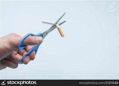 person s hand broking cigarette with scissor blue background