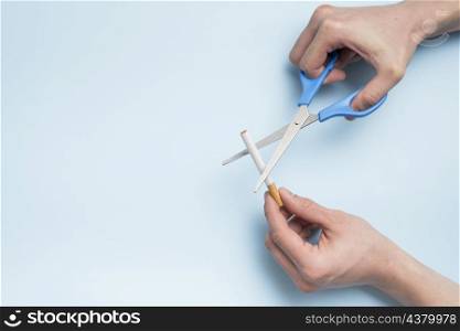 person s hand cutting cigarette with scissor blue background
