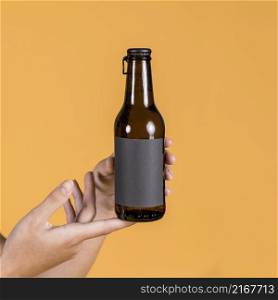 person s hand holding beer bottle yellow background