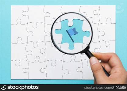 person s hand holding magnifying glass flag icon blue backdrop