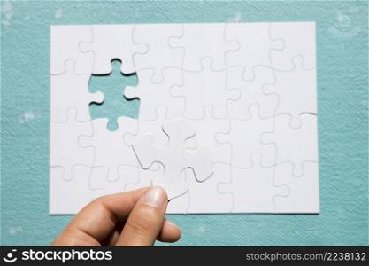 person s hand holding white puzzle piece puzzle grid blue textured background