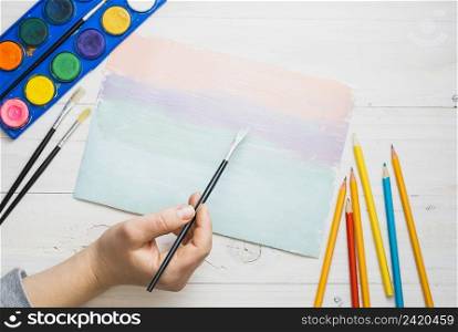 person s hand painting paper with paint brush watercolor desk