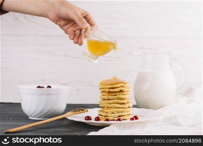 person s hand pouring honey delicious pancakes wooden table
