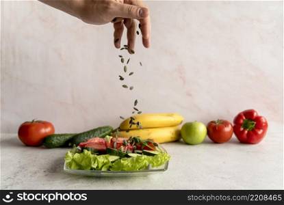 person s hand sprinkling pumpkin seeds vegetable salad