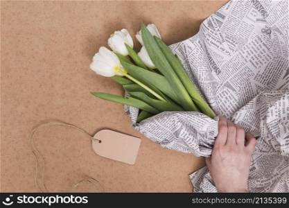 person s hand wrapping white tulip flowers newspaper with price tag brown background