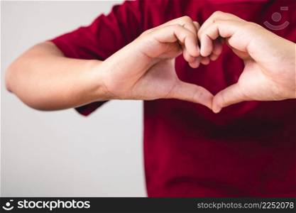 Person shows hands sign of love near the chest. The man with red shirt in medium close up shot. Valentine&rsquo;s concept. Copy space for messages, words and texts.