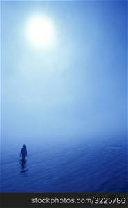 Person Standing In Water Under A Thick Sunlit Sky