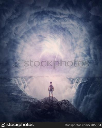 Person stands on the edge of a cliff above a waterfall looking at a huge whirlwind in the clouds that creates a portal to another planet. Surreal and fantasy scene, magical world adventure concept