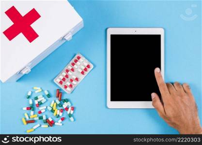 person using digital tablet with first aid kit capsules blue background