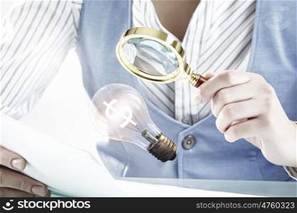 Person using magnifier for exploration. Young businessman looking in magnifying glass at light bulb