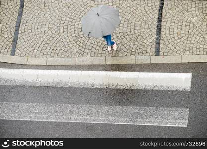 Person walking on city street during rainy day holding umbrella protecting from rain. High angle top view.. Person holding umbrella on street.