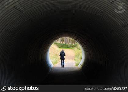 Person walks through a dark tunnel into the light at the end of the tunnel