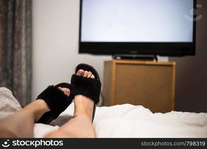 Person watches TV at night in his bed with his feet wearing black Flip Flops. The TV screen is blank white in her bedroom. Person watches TV at night in his bed with his feet wearing black Flip Flops. The TV screen is blank white