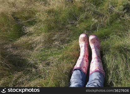 Person wearing pink galoshes lying in grass, low section