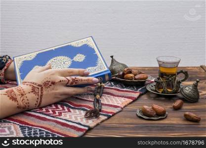 person with mehndi holding quran near tea glass
