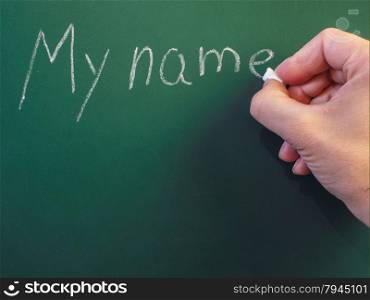Person writing on green chalkboard; My name, with chalk