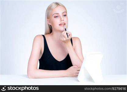 Personable young woman with flawless healthy skin and natural makeup putting fashion glossy lipstick on her lip with lip brush in isolated background. Facial cosmetic makeup in process.. Personable young woman putting alluring fashion glossy lipstick.