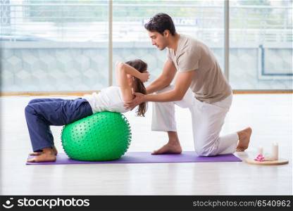 Personal coach helping woman in gym with stability ball