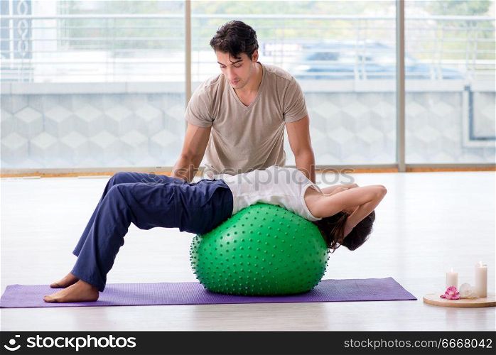 Personal coach helping woman in gym with stability ball
