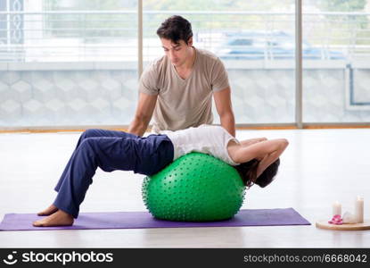 Personal coach helping woman in gym with stability ball