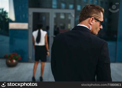 Personal guard in sunglasses and security earpiece, back view, black business woman on background. Bodyguard is a risky profession, protection of VIPs, guarding