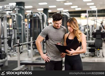 Personal trainer and client looking at his progress at the gym. Athletic man and woman wearing sportswear.