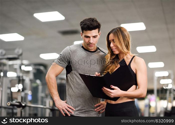Personal trainer and client looking at his progress at the gym. Athletic man and woman wearing sportswear.