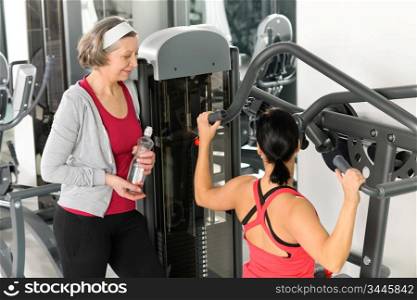 Personal trainer at fitness center showing exercise to senior woman