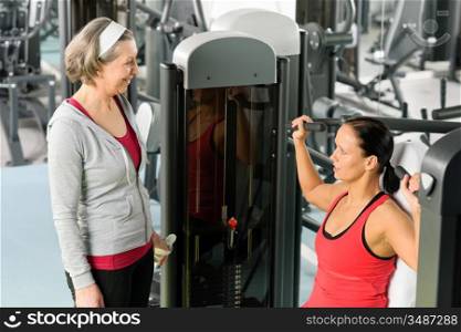 Personal trainer at fitness center showing exercise to senior woman