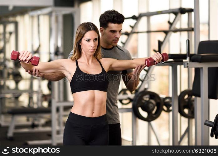 Personal trainer helping a young woman lift dumbells while working out in a gym