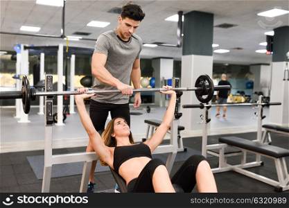 Personal trainer helping a young woman lift weights while working out in a gym