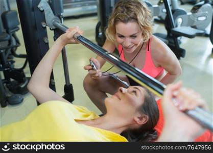 personal trainer helping woman lift a barbell