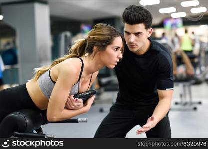 Personal trainer helping young woman lift weights while working out in a gym