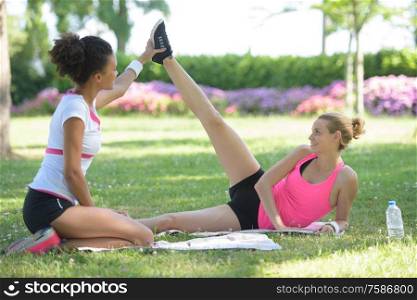 personal trainer holding leg of woman stretching in park