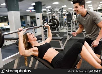 Personal trainer motivating a young woman lift weights while working out in a gym