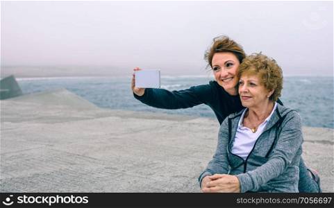 Personal trainer taking selfie with senior woman by sea pier. Trainer taking selfie with senior woman