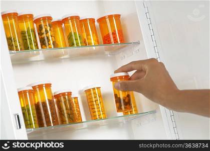Persons hand taking pill bottle from shelf
