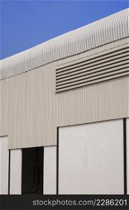 Perspective side view of corrugated steel with concrete wall of warehouse building structure is under construction against blue clear sky in vertical frame
