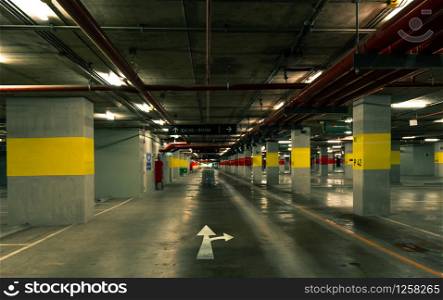 Perspective view of empty indoor car parking lot at the mall. Underground concrete parking garage with open lamp at night. White direction sign. Choose way to live your life. Wiring and plumbing.