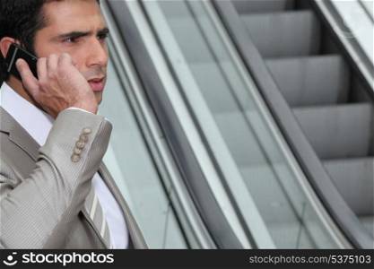 Perturbed businessman using a cellphone by an escalator