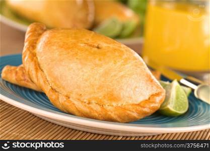 Peruvian snack called Empanada (pie) filled with chicken and beef served with limes (Selective Focus, Focus on the middle front part of the empanada)