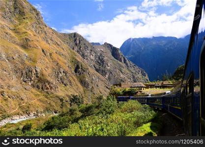 Peruvian train to Machu Picchu passes ancient buildings along the Urubamba River.
