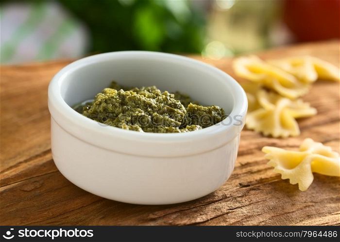Pesto alla genovese made of basil, garlic, olive oil, pine nuts and cheese, traditional sauce for pasta in the Italian cuisine, photographed on wood with natural light (Selective Focus, Focus in the middle of the pesto)