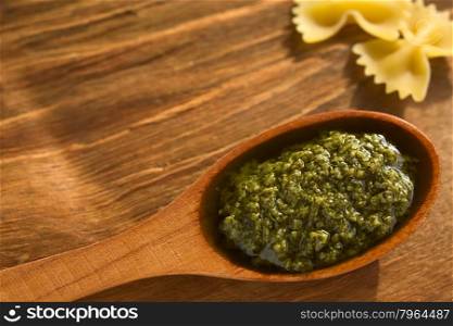 Pesto alla genovese made of basil, garlic, olive oil, pine nuts and cheese, traditional sauce for pasta in the Italian cuisine, photographed on wood with natural light (Selective Focus, Focus in the middle of the pesto)