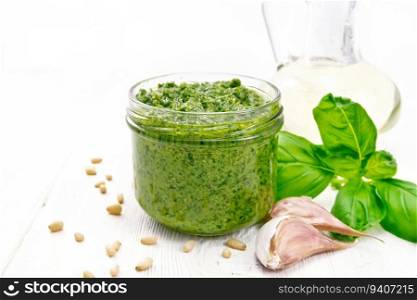Pesto sauce in a glass jar, basil, pine nuts, garlic and olive oil on white wooden board background