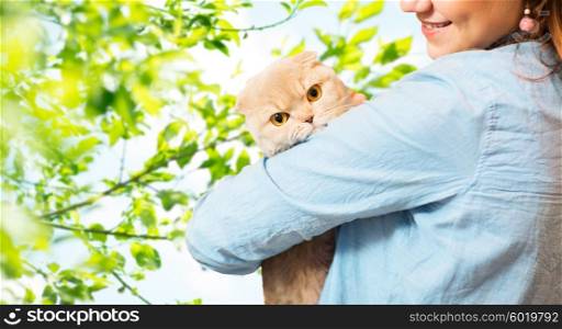 pet, animals, care and people concept - close up of happy woman holding scottish fold kitten over natural green background