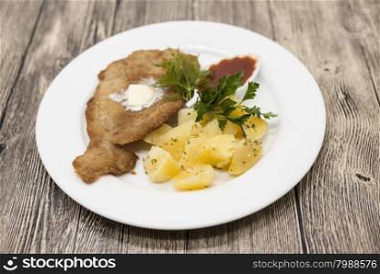 Petite Wiener schnitzel with boiled potatoes and ketchup. Served on a white porcelain plate on a wooden background.. Petite Wiener schnitzel with boiled potatoes and ketchup. Served on a white porcelain plate on a wooden background