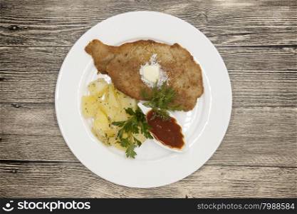 Petite Wiener schnitzel with boiled potatoes and ketchup. Served on a white porcelain plate on a wooden background.. Petite Wiener schnitzel with boiled potatoes and ketchup. Served on a white porcelain plate on a wooden background