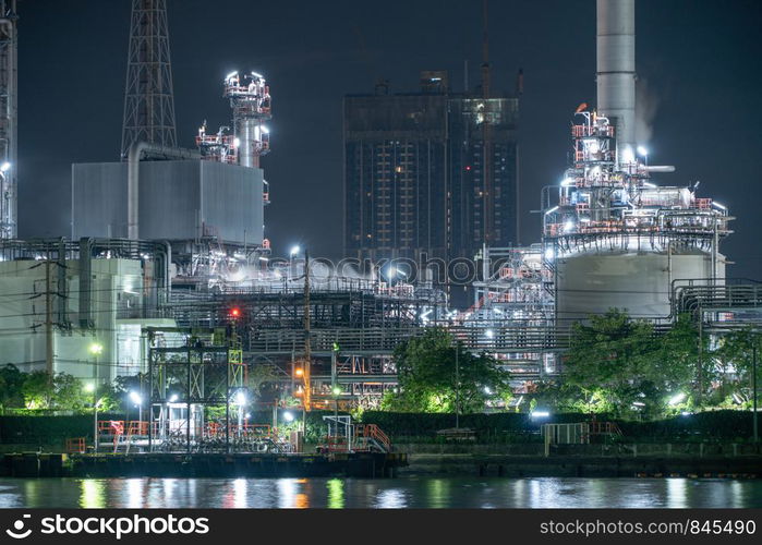 Petrochemical oil refinery and sea in industrial engineering concept in Bangna district, Bangkok, Thailand. Oil and gas tanks pipelines in industry. Modern metal factory at night.