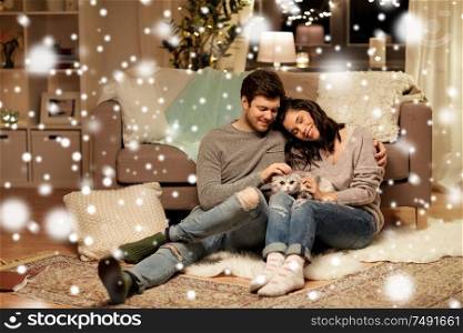 pets, christmas and people concept - happy couple with cat at home over snow. happy couple with cat at home